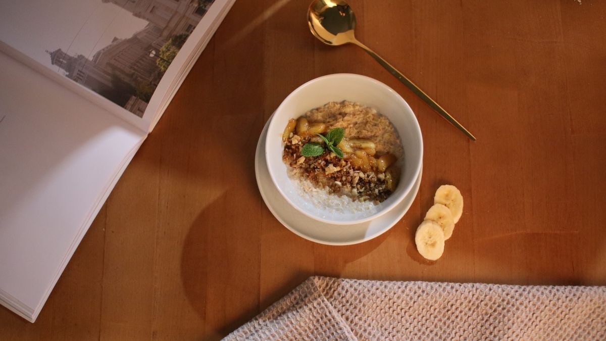 Warm oatmeal with granola and banana slices on a wooden table for a perfect breakfast.