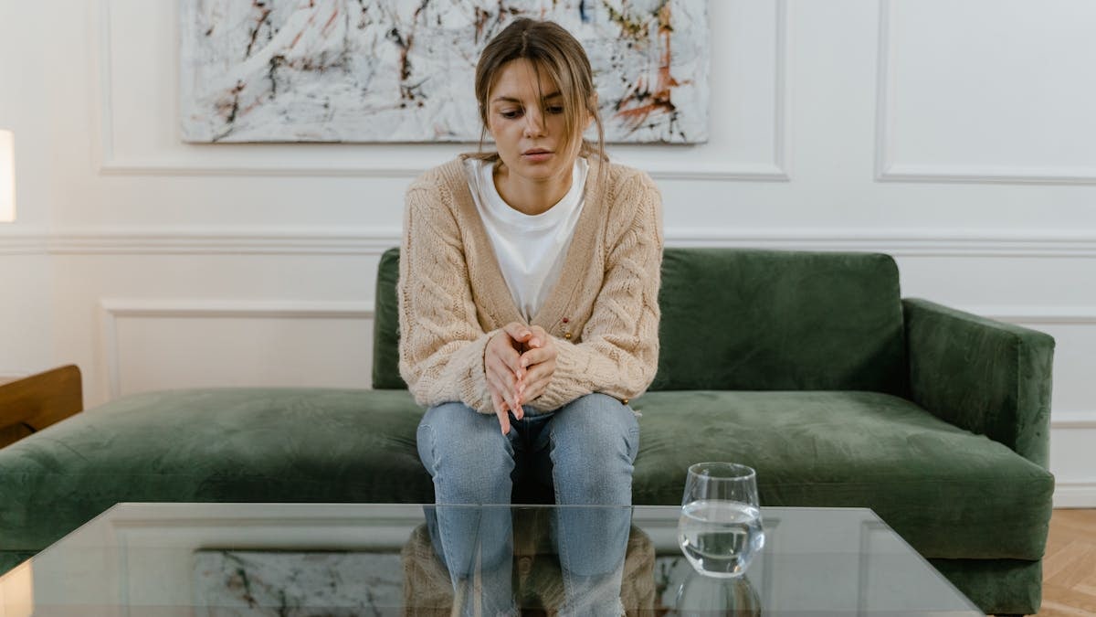 Woman sitting on a green sofa with a pensive expression, reflecting indoors.